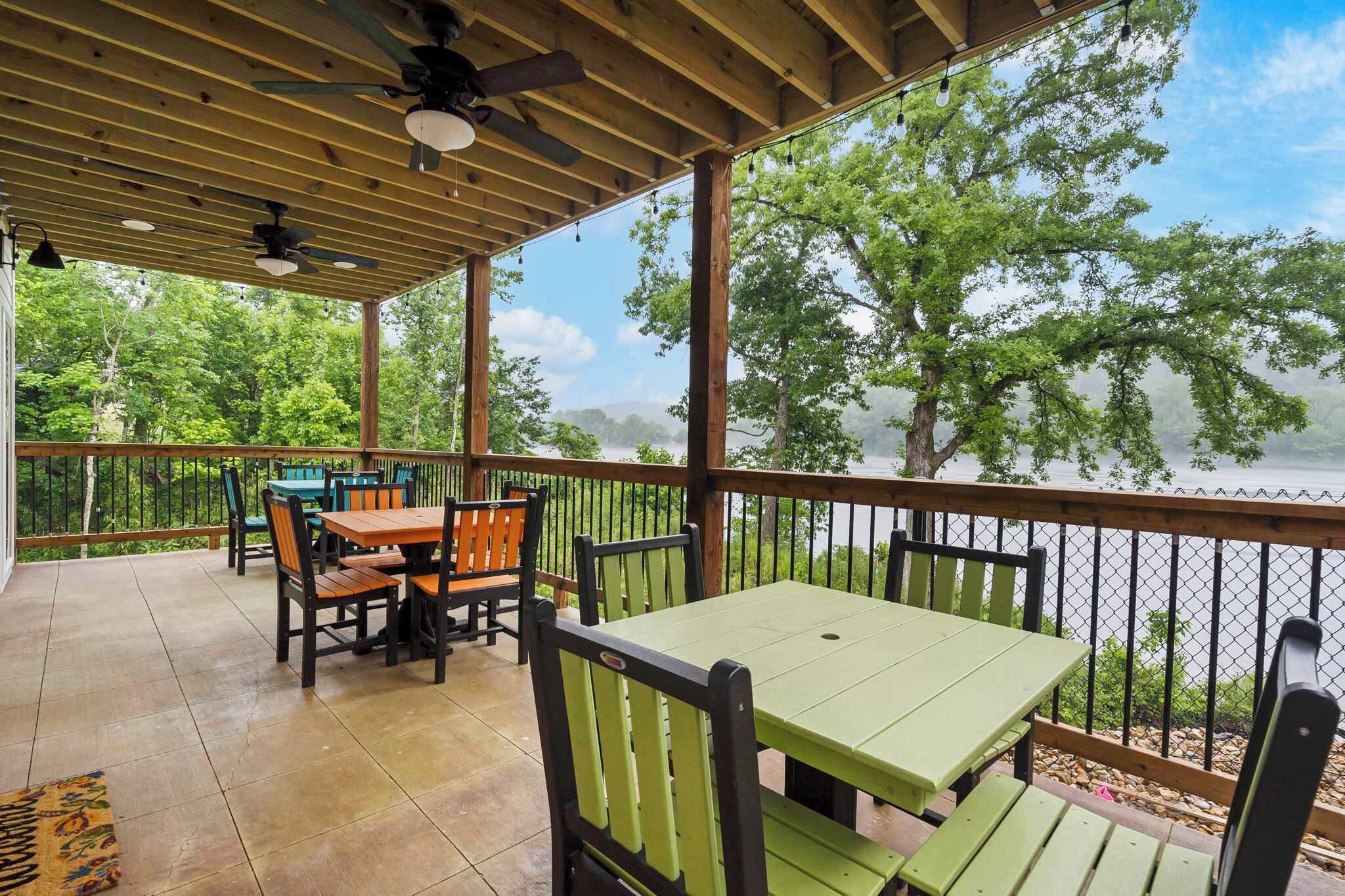 A covered outdoor patio with wooden tables and chairs, overlooking a body of water and trees.