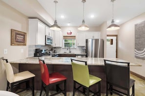 A kitchen with white cabinets, a stainless steel refrigerator, a coffee sign, and pendant lights.