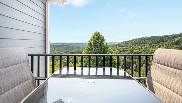 A balcony with a table and chairs, overlooking a forested landscape. - Our Happy Place in the Heart of Branson (Branson)