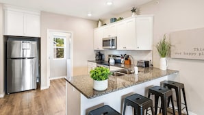 A modern kitchen with white cabinets, stainless steel appliances, a granite countertop, and a small island with bar stools. - Our Happy Place in the Heart of Branson (Branson)