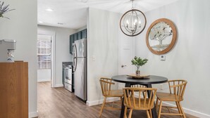 Een moderne keuken met roestvrijstalen apparatuur, een eetgedeelte met een ronde tafel en houten stoelen, en een decoratieve spiegel in de vorm van een boom aan de muur.