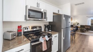 A modern kitchen with white cabinets, stainless steel appliances, a granite countertop, and a dining area with a brown leather couch and a coffee table. - *New Listing* Vineyard Valley Views | Balcony (Branson)