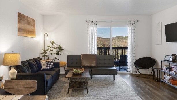A living room with a sofa, armchair, and coffee table, a TV on the wall, and a balcony with curtains. - *New Listing* Vineyard Valley Views | Balcony (Branson)