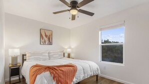A bedroom with a bed, a ceiling fan, bedside lamps, a window with a view, and a painting on the wall. - *New Listing* Vineyard Valley Views | Balcony (Branson)