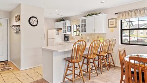 A modern kitchen with white cabinets, a central island with bar stools, and a dining table. - The Greens Escape in Branson | Near DT! (Branson)