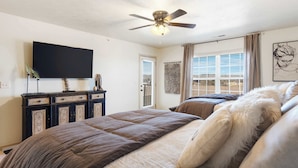 A bedroom with a bed, a ceiling fan, a TV, and a window with curtains. - Par 7 Penthouse at StoneBridge Resort (Branson West)