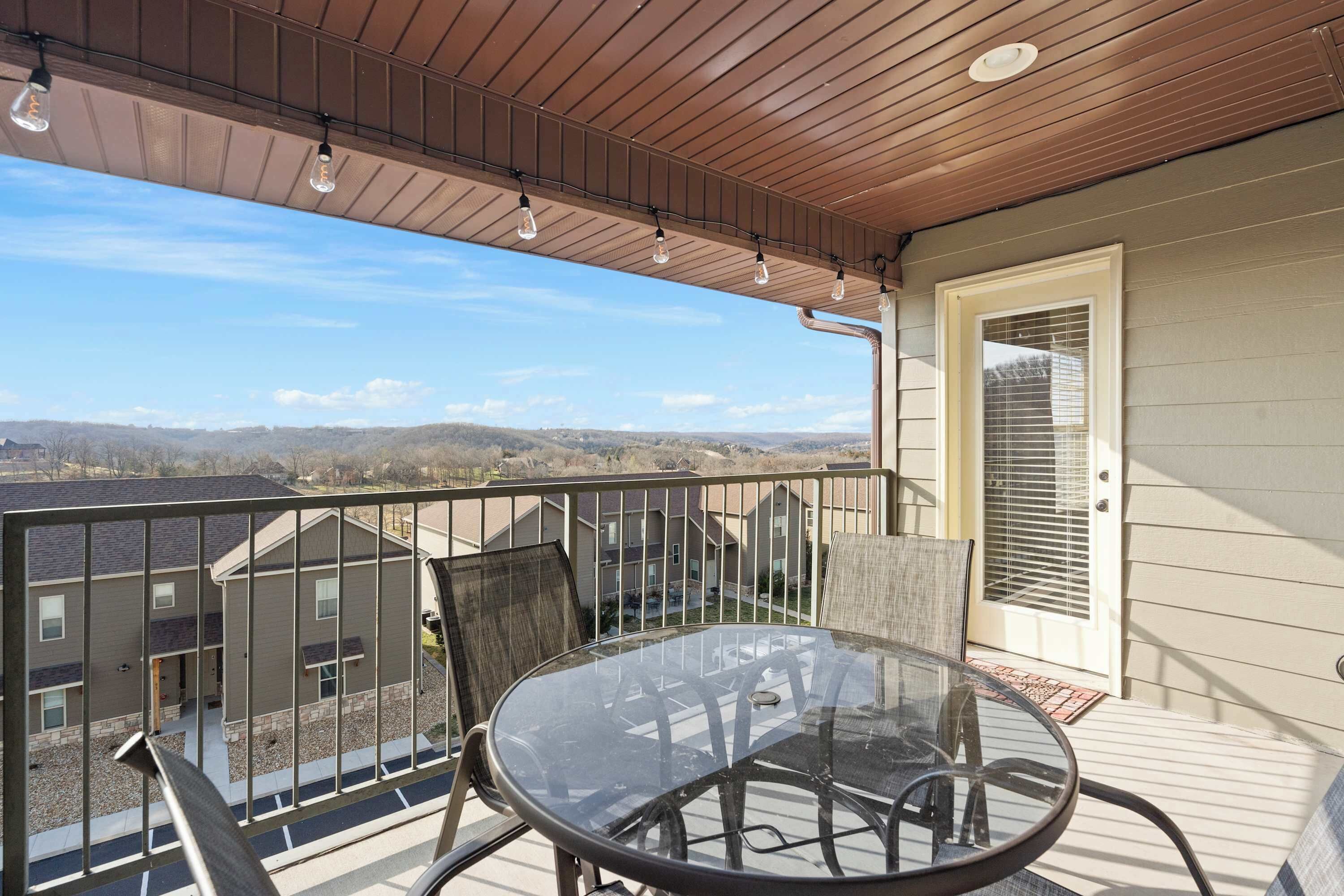 Un balcón con una mesa y sillas de vidrio, con vistas a una zona residencial con casas y un cielo despejado.