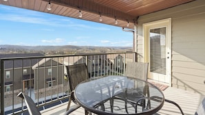 A balcony with a glass table and chairs, overlooking a residential area with houses and a clear sky. - Par 7 Penthouse at StoneBridge Resort (Branson West)