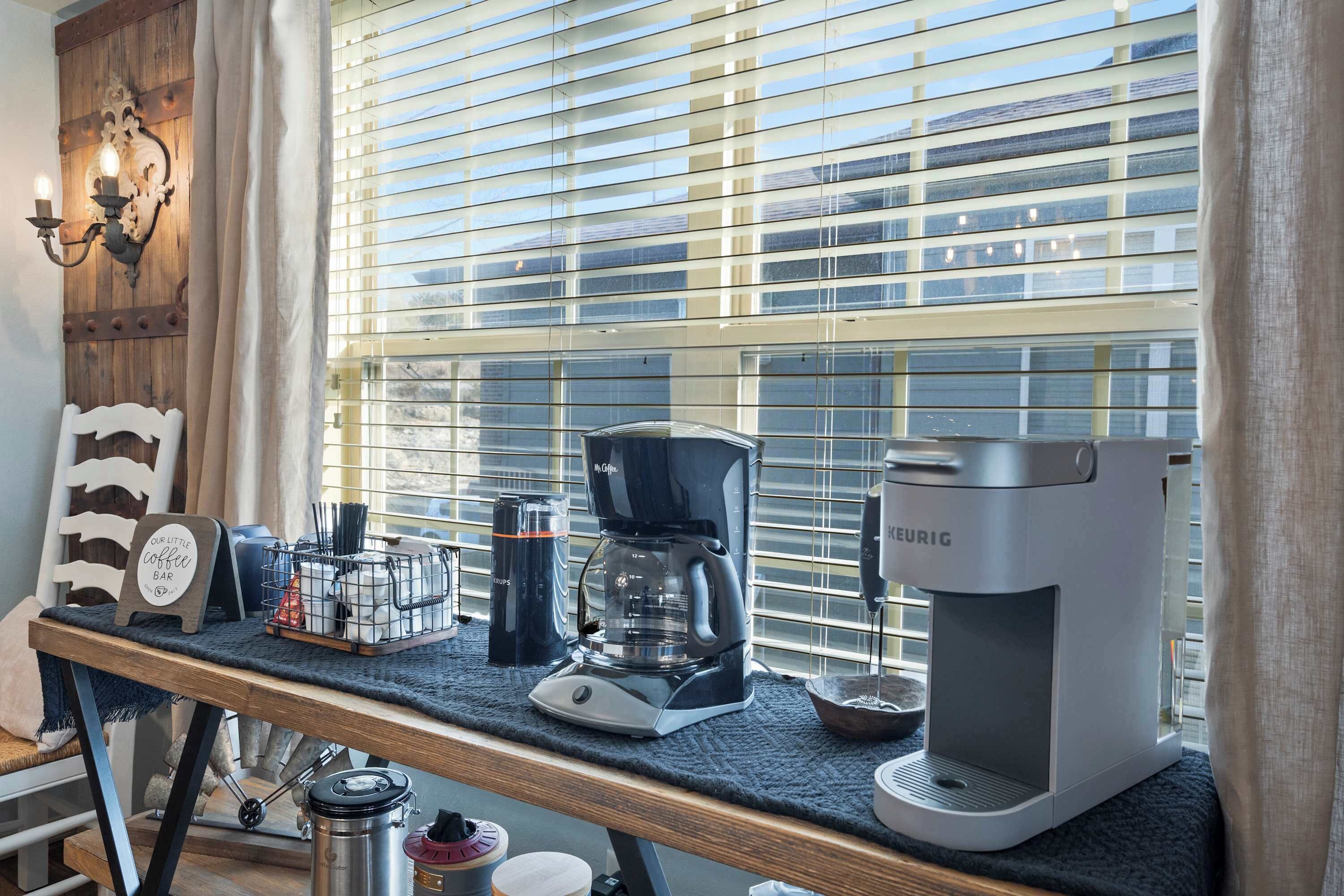 A kitchen counter with a coffee maker, a kettle, and a sign that reads "Our Little Coffee Bar".