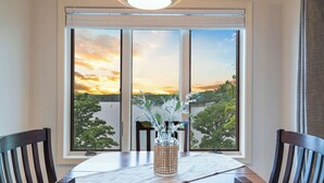 A dining table with a view of a sunset through large windows, a decorative vase with plants, and wooden chairs. - Lakefront Oasis – Amazing Views! (Kimberling City)