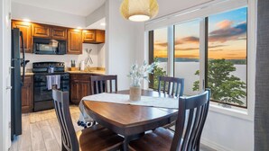A modern kitchen with wooden cabinets, a black stove, and a dining area with a wooden table and chairs. - Lakefront Oasis – Amazing Views! (Kimberling City)