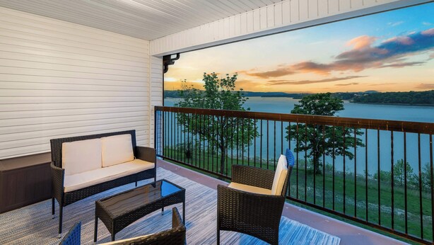 A balcony with wicker furniture, a view of a lake at sunset, and a railing. - Lakefront Oasis – Amazing Views! (Kimberling City)