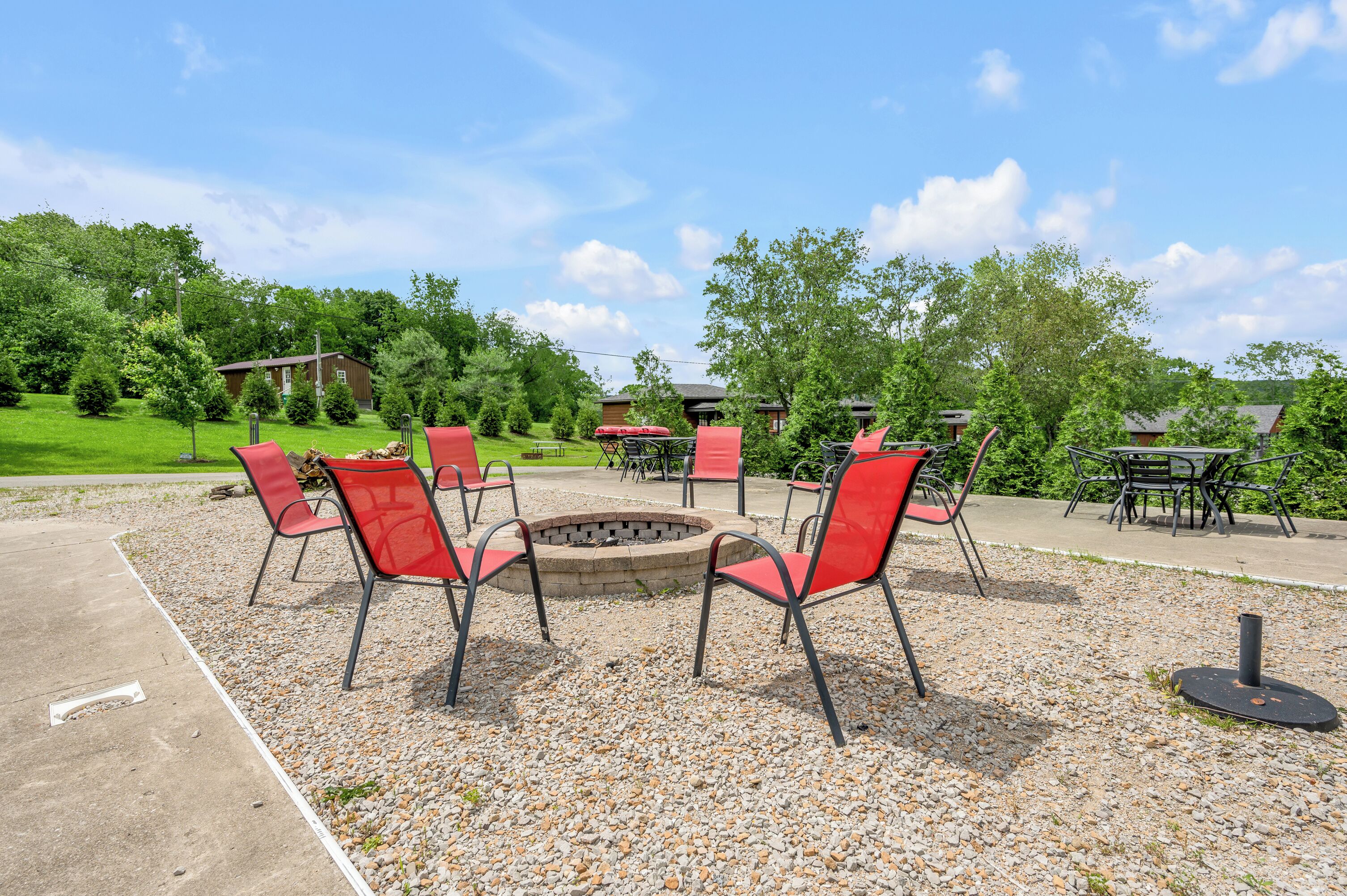 Un espace extérieur aménagé avec des chaises et des tables rouges, un foyer et un sol recouvert de gravier.
