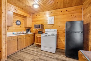 Une cuisine aux murs lambrés, équipée d’un four à micro-ondes, d’une cuisinière, d’un réfrigérateur et de meubles de rangement en bois.