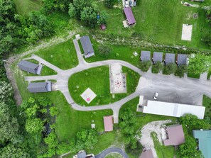 Vue aérienne d’un quartier résidentiel comprenant plusieurs maisons, une place centrale pavée et des espaces verts environnants.