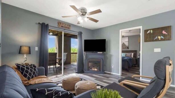 Una sala de estar con sofá, otomanas, una silla, chimenea, ventilador de techo y televisor.