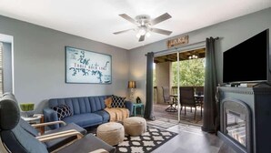 Una sala de estar moderna con un sofá azul, otomanes, una chimenea y un televisor.
