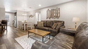 A living room with a brown leather sofa, a wooden coffee table, and a dining area with white chairs. - Rockwall Cottage | In the Heart of Branson! (Branson)