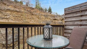 A glass table with a lantern on a deck with wooden railings and a chair. - Rockwall Cottage | In the Heart of Branson! (Branson)