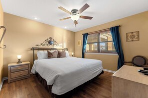 Un dormitorio con cama, mesita de noche, escritorio y ventilador de techo.