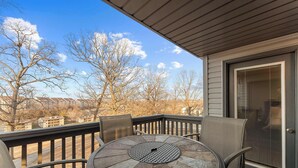 Un balcon avec une table ronde et des chaises, donnant sur un quartier résidentiel où les arbres sont sans feuilles et où se trouvent des maisons.