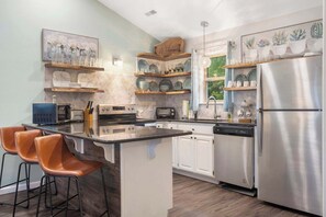 A modern kitchen with a central island, bar stools, stainless steel appliances, and decorative wall shelves.