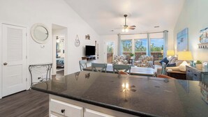 A spacious kitchen with a large island, a dining area with a table and chairs, and a living room with a sofa and a TV. - Retreat by Design | Resort Amenities (Branson West)