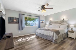 A bedroom with a bed, ceiling fan, window with curtains, artwork, and a TV. - Ozark Escape at the Pointe | Epic Nature (Branson)