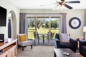 A living room with a sliding glass door to a patio, a ceiling fan, a television, and a coffee table. - Golf View Escape | Holiday Hills Branson | Golf | Outdoor Pools (Branson)