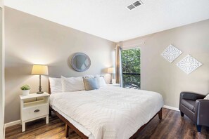 A bedroom with a bed, nightstand, lamp, potted plant, and decorative wall pieces.