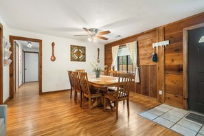 Un coin repas avec une table et des chaises en bois, un ventilateur de plafond et une fenêtre avec des rideaux.