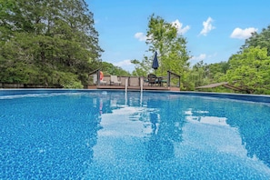 Une piscine aux eaux d’un bleu limpide, dotée d’un espace de détente et entourée d’arbres.