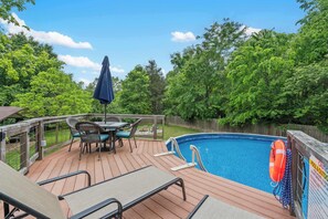 Une terrasse en bois avec une piscine, des chaises longues, une table et un parasol.