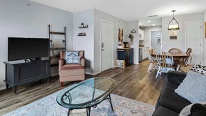 A modern living room with a TV, sofa, and glass coffee table. There is a dining area with a table and chairs. - Family-Friendly Retreat – Enviable Location! (Branson)