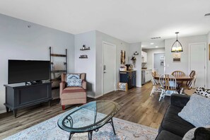 Ett modernt vardagsrum med en platt-TV, ett soffbord i glas, en soffa och en matplats med ett bord och stolar i trä.