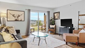 A living room with a sofa, a glass coffee table, a TV, and a view of the outdoors. - Family-Friendly Retreat – Enviable Location! (Branson)
