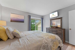 A bedroom with a bed, a dresser, a painting, and a view of the outdoors. - *Newly Updated* Mulligans Escape | Community Pool (Branson)