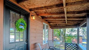 A wooden porch with a covered area, a door with a wreath, and two chairs.