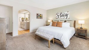 Ein Schlafzimmer mit einem großen Bett, einer Bank, einem Nachttisch und einem Wandzeichen.