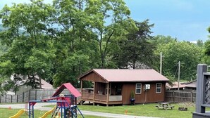 Ein Spielplatz mit Rutschen und einer Spielanlage, ein Holzgebäude mit Veranda und ein Picknicktisch.