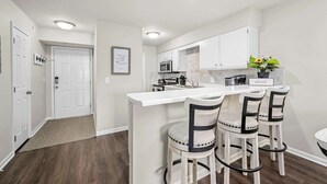Une cuisine moderne avec des meubles blancs, un îlot central doté de tabourets de bar et une petite table à manger.