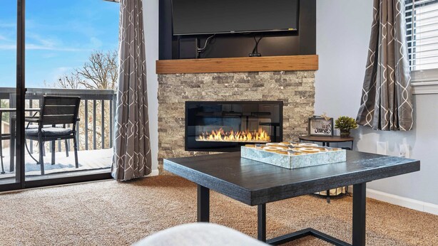 Una sala de estar moderna con chimenea de piedra, un televisor de pantalla plana montado encima y una mesa de comedor con una bandeja de pan.