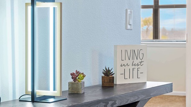A modern room with a standing lamp, two small potted plants, and a motivational quote sign on a wooden table. - Legacy View at Pointe - Branson (Branson)