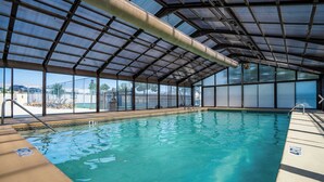 Una piscina interior con agua cristalina, rodeada por un espacio techado con ventanales amplios.