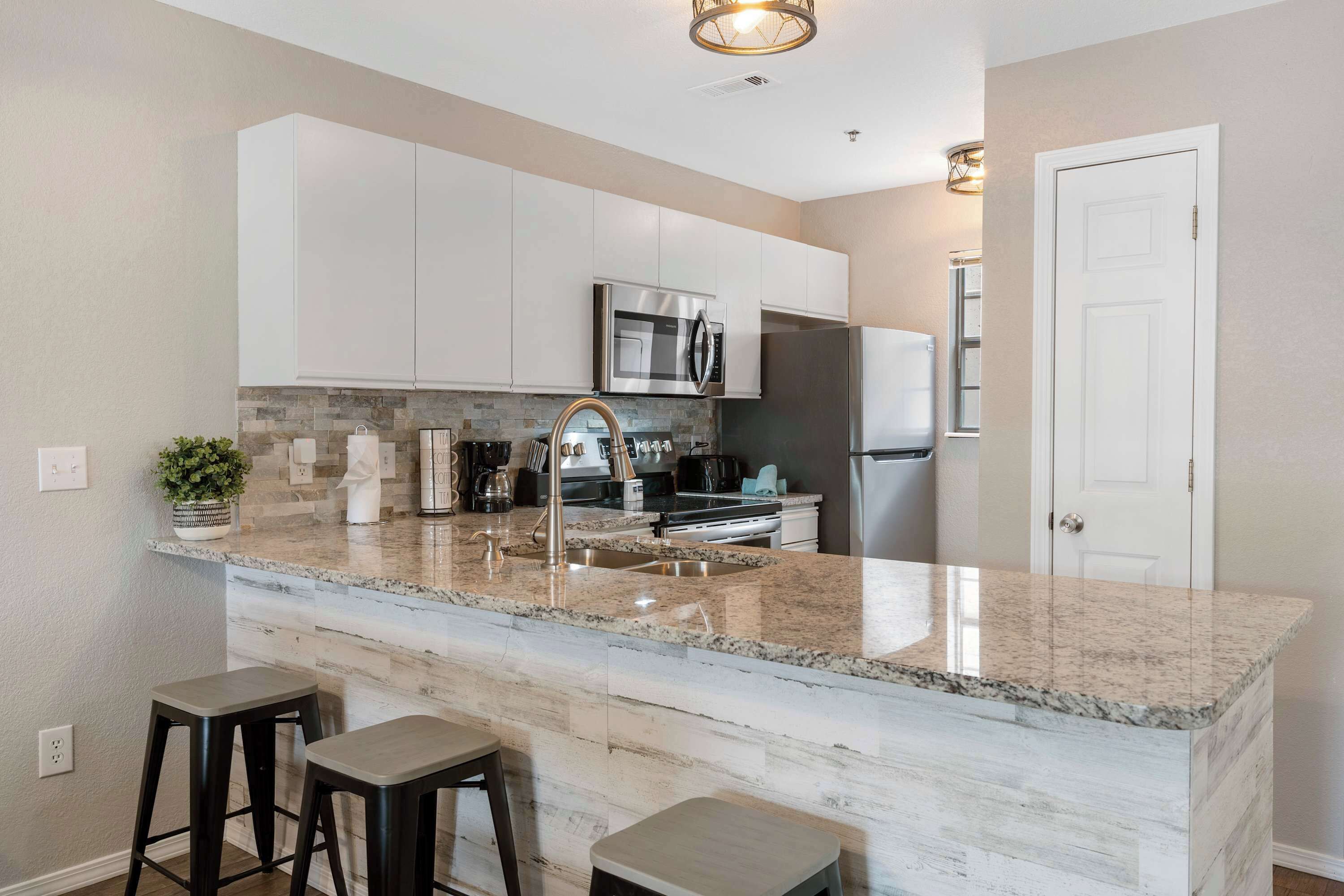 A modern kitchen with white cabinets, granite countertops, stainless steel appliances, and two bar stools.