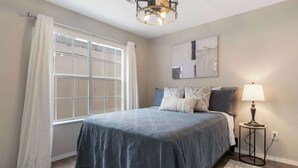 A bedroom with a large bed, a window with curtains, a bedside lamp, and a rug. - The Branson Condo at Fall Creek | Overlooking the Rolling Hills (Branson)
