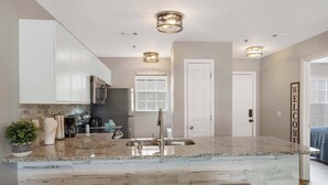 A modern kitchen with a marble countertop, stainless steel appliances, and a built-in sink. There are three stools and a potted plant on the counter. - The Branson Condo at Fall Creek | Overlooking the Rolling Hills (Branson)