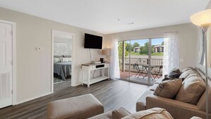 A modern living room with a sofa, a flat-screen TV, and a balcony with outdoor furniture. - The Branson Condo at Fall Creek | Overlooking the Rolling Hills (Branson)