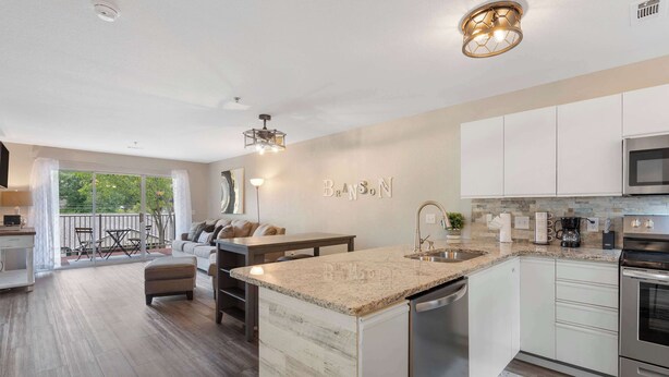 A modern kitchen with a central island, white cabinetry, and a large window overlooking a balcony. - The Branson Condo at Fall Creek | Overlooking the Rolling Hills (Branson)