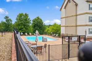 A swimming pool with lounge chairs and umbrellas, surrounded by a fence and trees. - Kings Hideaway | Near DT! (Branson)